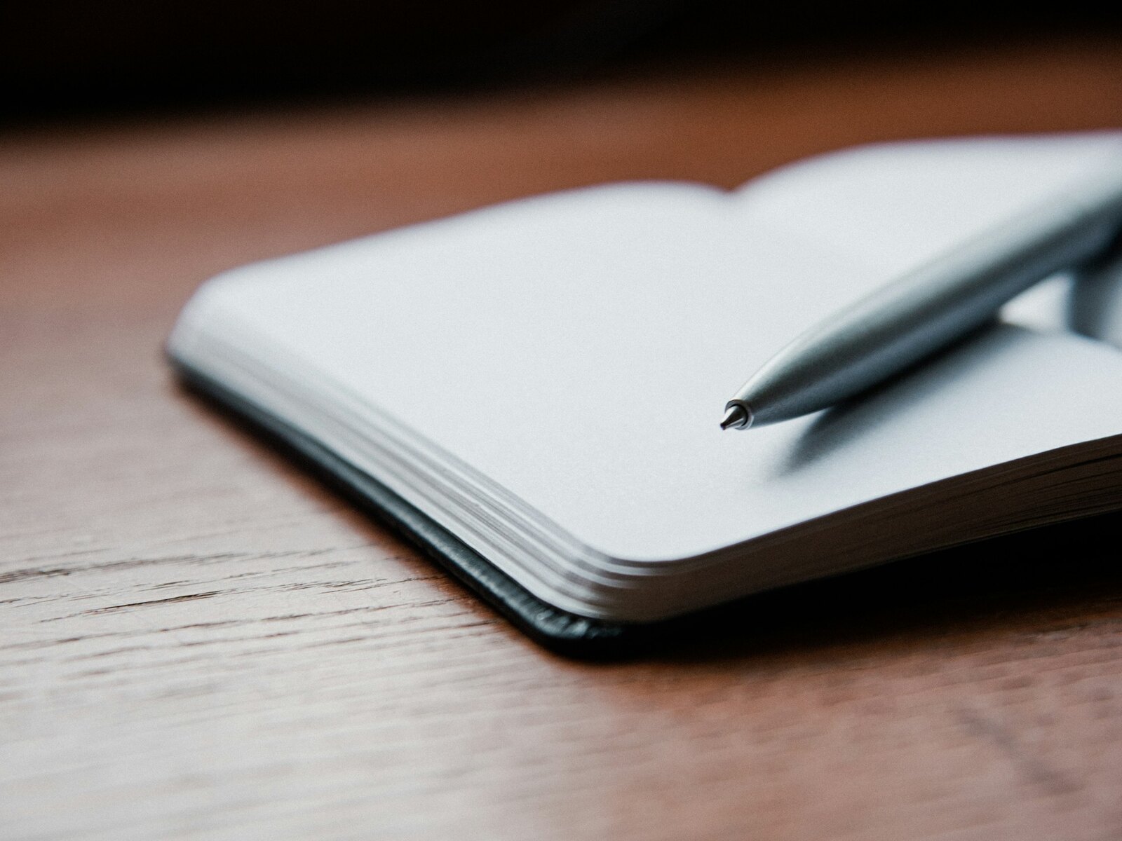 An open notebook and pen on a light wooden desk